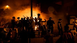 In this May 28, 2020, file photo, protesters cheer as the Third Police Precinct burns behind them in Minneapolis, Minnesota.