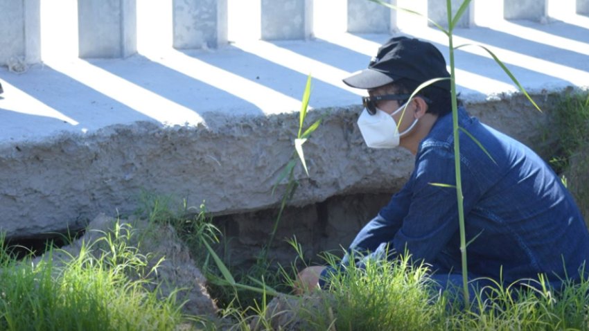 hombre inspeccionando erosion en cimiento de muro fronterizo