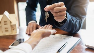 Una persona dando una llave con contrato firmado.