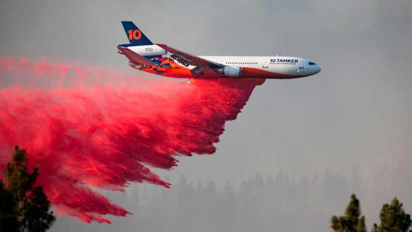 A DC-10 tanker drops red retardant over a forest.