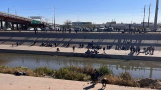 Fotografía tomada desde la valla fronteriza de El Paso, Texas, donde se muestra a varios migrantes esperando para cruzar el río en la zona de Ciudad Juárez, México.