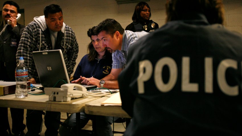 Los Angeles Police Department officers and detectives crowd around a laptop computer at a makeshift booking area inside 77th Street police station garage after raiding several LA locations Thursday morning March 6 2008. The raids netted more than twodozen suspects in an alleged auto insurance fraud ring.  (Photo by Brian Vander Brug/Los Angeles Times via Getty Images)