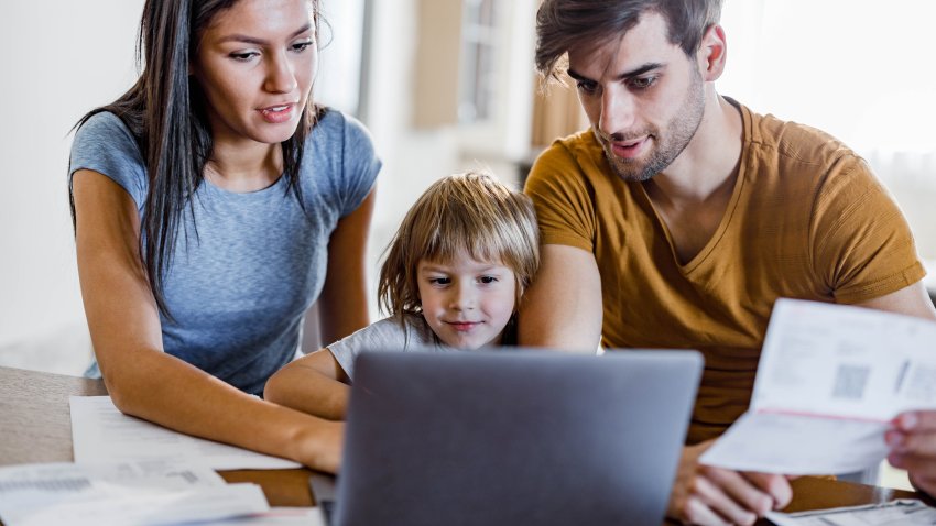 Young happy parents and their small son using laptop at home.