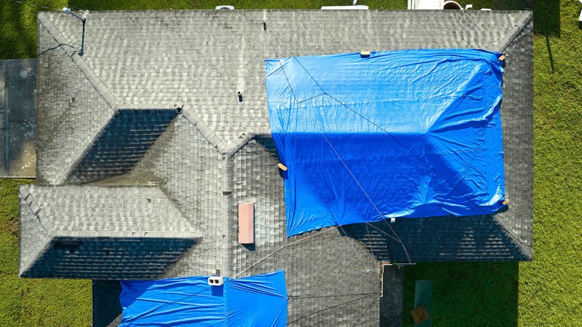 Aerial view of damaged in hurricane Ian house roof covered with blue protective tarp against rain water leaking until replacement of asphalt shingles