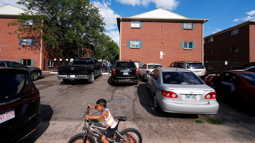 ARCHIVO – Un niño anda en bicicleta frente a edificios de apartamentos mientras en el jardín se lleva a cabo una junta organizada por el Colectivo Comunitario de East Colfax, ello con el fin de atender problemas crónicos en esos edificios ocupados por personas desplazadas de sus países en Centro y Sudamérica, el 3 de septiembre de 2024, en Aurora, Colorado. (AP Foto/David Zalubowski, archivo)