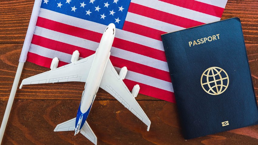 Flag of United States with passport and toy airplane on wooden background. Flight travel concept
