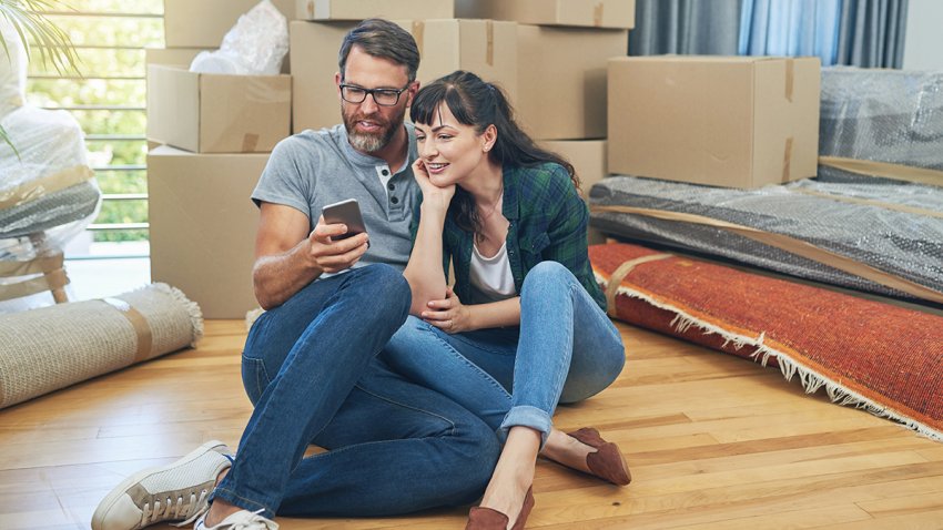 Couple, moving and happy browsing on smartphone, smile and ecommerce for apartment purchase on website. Living room, floor and rent payment on banking fintech app, people and property or new home
