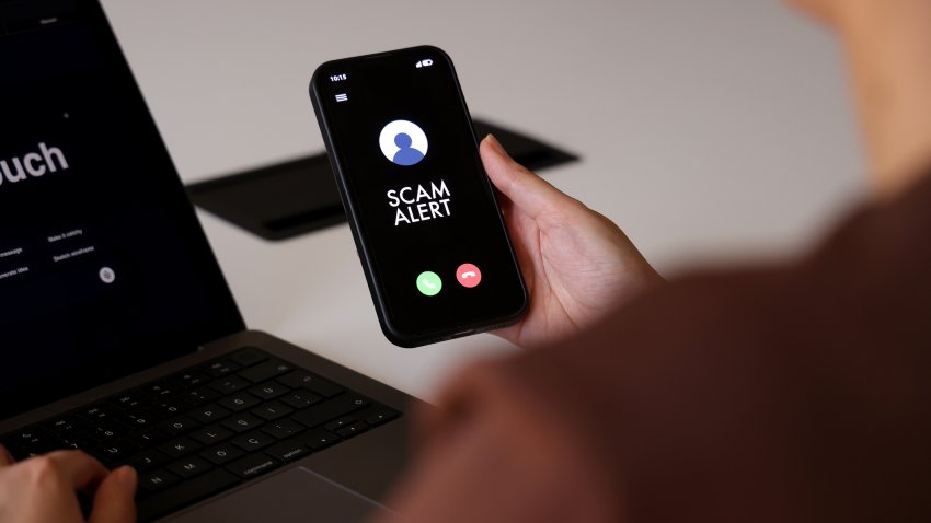 A person holds a smartphone displaying a “Scam Alert” message on an incoming call screen. The dark interface clearly indicates a fraud warning, conveying concerns about cybersecurity, mobile fraud, and digital safety. The indoor environment and close-up composition highlight the immediacy and relevance of online threat awareness in everyday mobile use.